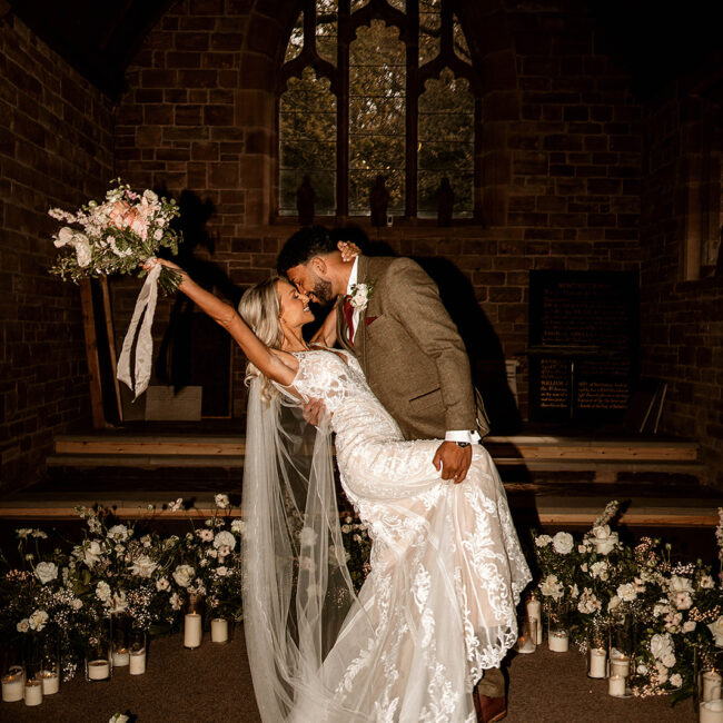 Bride and groom, doing a deep dip after getting married. Surrounded by a floral nest and bride holding bouquet in the air.