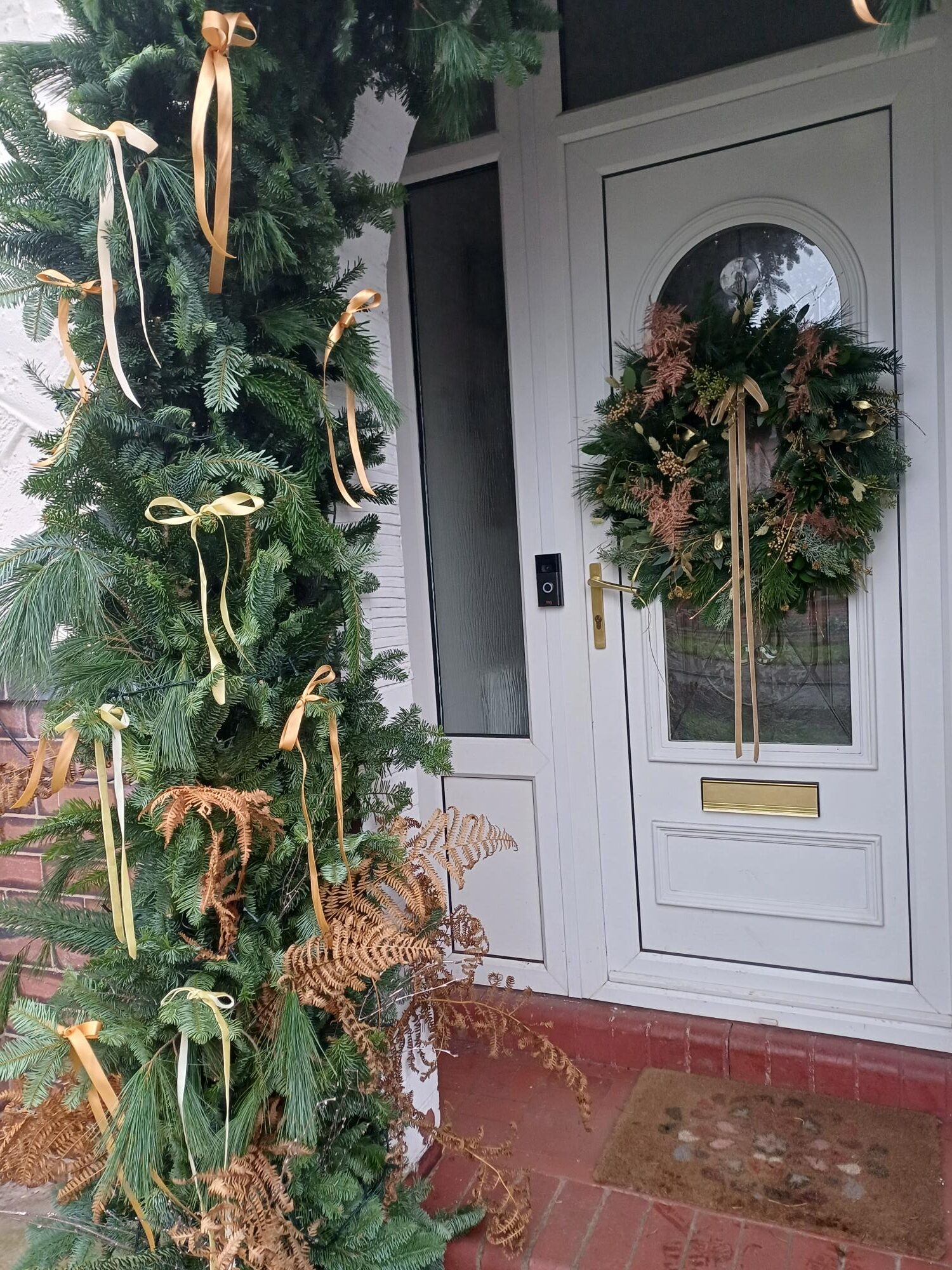 A Bespoke fresh Foliage Christmas Door Installation Arch with gold bows and lights.